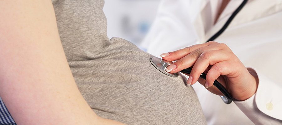 Médica ouve coração de bebê com estetoscópio em mulher grávida