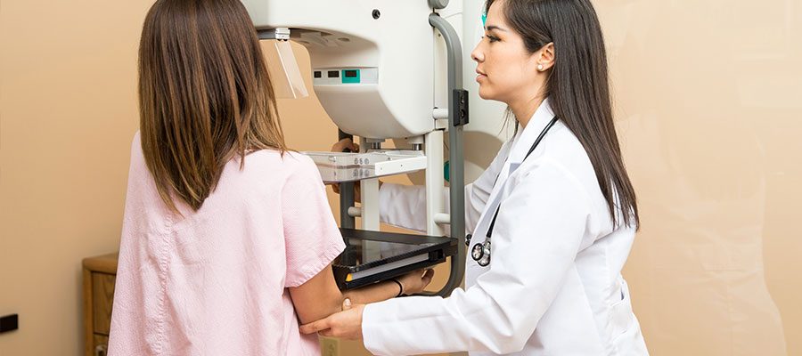 Paciente realiza exame de mamografia com ajuda de médica