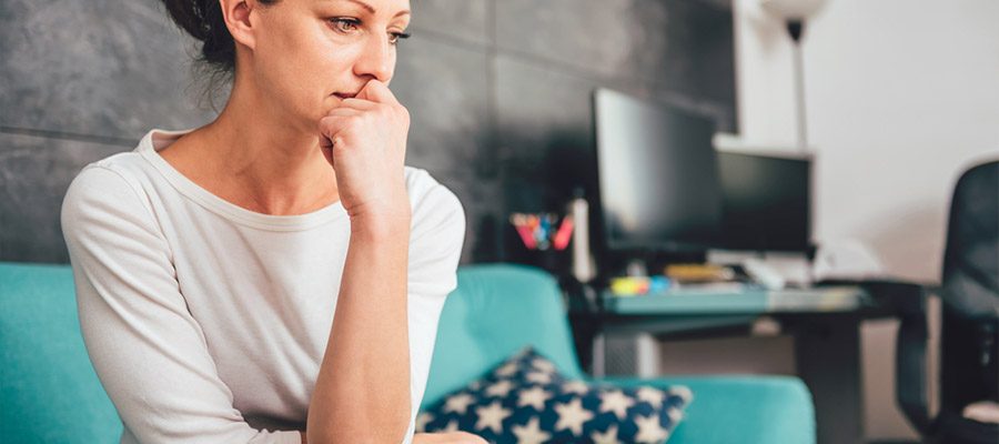 Mulher triste e preocupada sentada em sofá azul após diagnóstico de câncer de mama