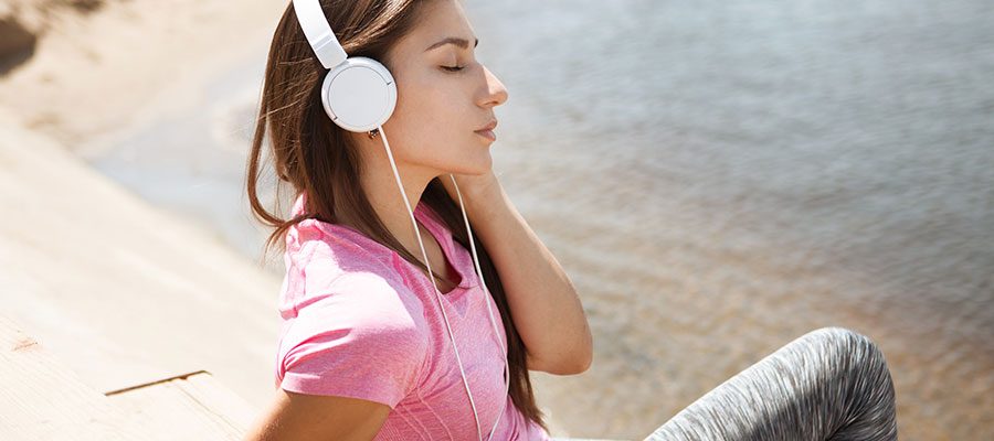 Mulher jovem morena escuta música com fones de ouvido em frente a um lago