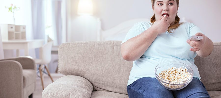 Mulher acima do peso come pipoca enquanto vê televisão
