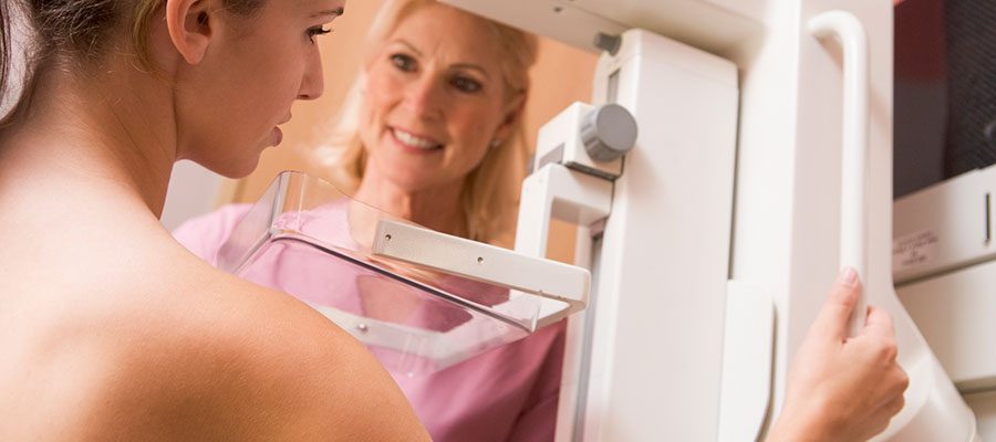 Mulher jovem realiza mamografia com ajuda de radiologista