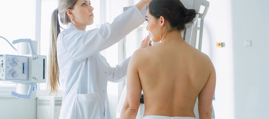 Mulher com cabelo preto e de toalha se preparando para realizar exame de mamografia