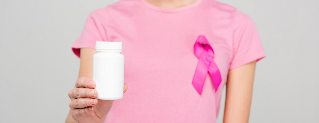 Mulher de camiseta e laço rosa segurando frasco de remédio