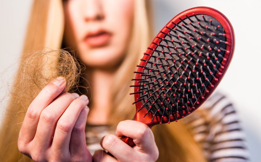 Mulher segurando escova de cabelo com fios soltos