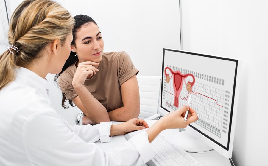 Ginecologista se comunica com sua paciente, indicando o ciclo menstrual no monitor