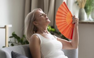 Mulher na menopausa com ondas de calor na frente de um ventilador