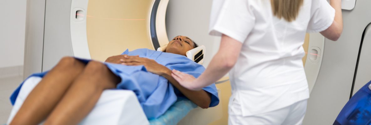Profissional de saúde em pé, ao lado de homem negro fazendo radioterapia