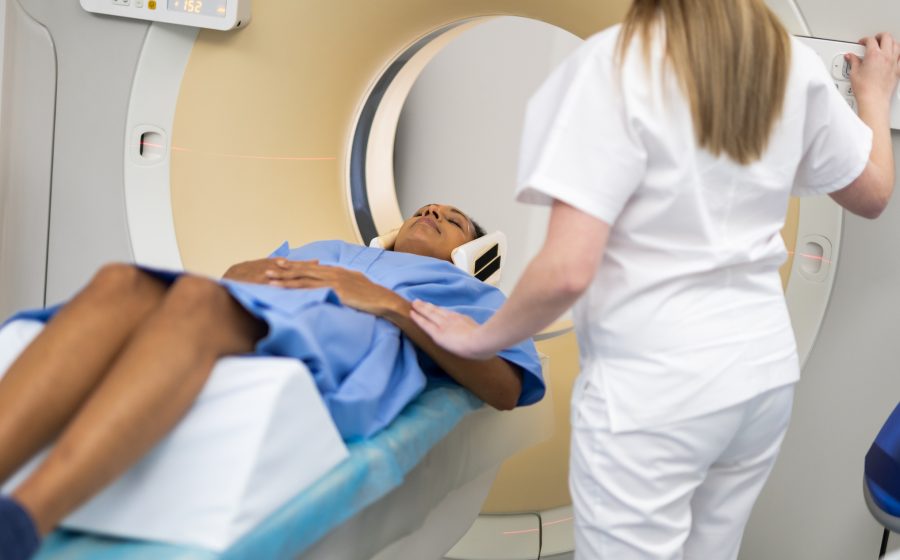 Profissional de saúde em pé, ao lado de homem negro fazendo radioterapia