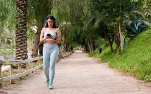 Mulher de roupas esportivas anda segurando um telefone em um parque da cidade