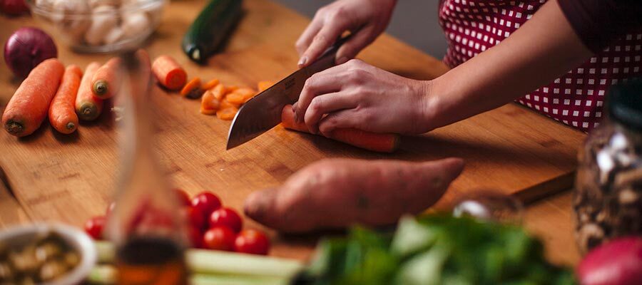 Mulher fatiando alimentos de uma dieta vegetariana, como cenoura